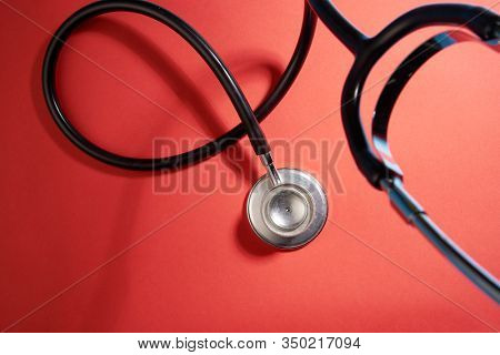 black stethoscope on a red background top view with copy space.