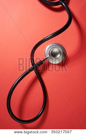 black stethoscope on a red background top view with copy space.