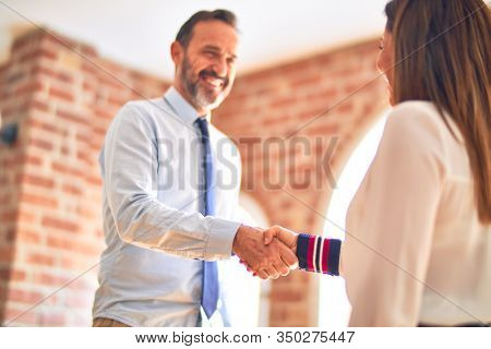 Two middle age business workers smiling happy and confident. Working together with smile on face doing handsake at the office