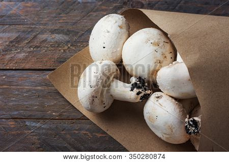 Bunch Of Freshly Picked White Button Mushrooms In Brown Kraft Paper Bag On Rustic Wood Table. Plasti