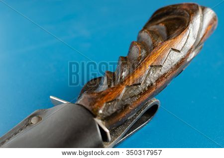 Wooden Hilt Of An Old Hunting Knife On A Blue Background. The Knife Is Hidden In Black Leather Scabb