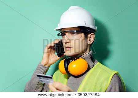 Studio Portrait Of Young Builder Man, Engineer, Pay With Credit Card By Phone. Wearing Construction 