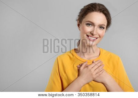 Beautiful Grateful Woman With Hands On Chest Against Light Grey Background. Space For Text