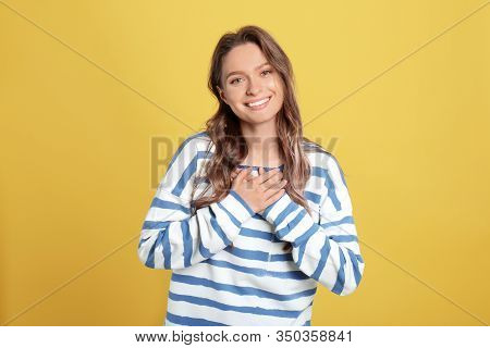Beautiful Grateful Woman With Hands On Chest Against Yellow Background