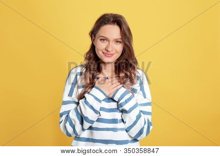 Beautiful Grateful Woman With Hands On Chest Against Yellow Background