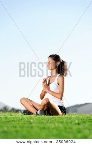 สงบ meditating ขณะนั่งอยู่บนหญ้าข้าม legged ผู้หญิงเซน หลักโยคะเซน