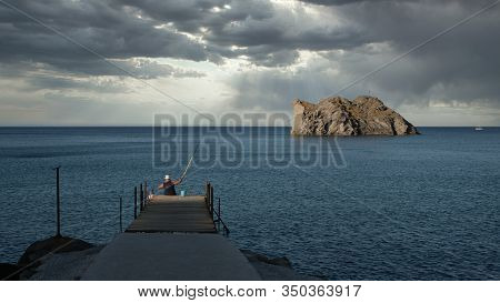 Fisherman Sitting On A Delapidated Dock On A Stormy Day With Island In The Background On The Island 