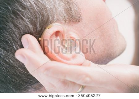 Man wearing deaf aid in ear attempting to hear something