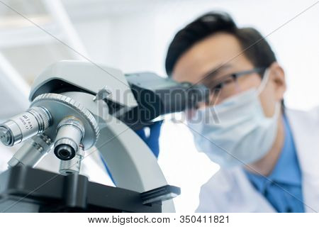 Unrecognizable male pharmacologist examining specimen using microscope in modern laboratory, horizontal shot