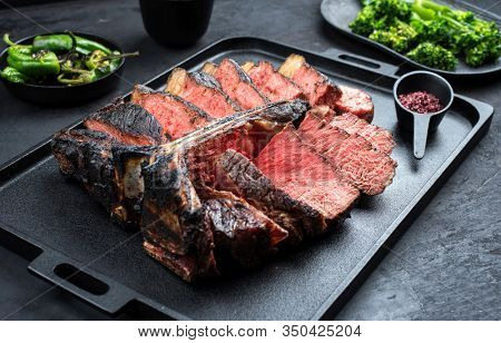 Barbecue dry aged wagyu porterhouse beef steak sliced with large fillet piece with hot chili and rapini broccoli rabe as closeup on a modern design black cast iron tray 