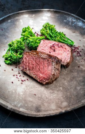 Barbecue dry aged wagyu roast beef natural sliced offered with rapini and salt as closeup on a modern design plate 