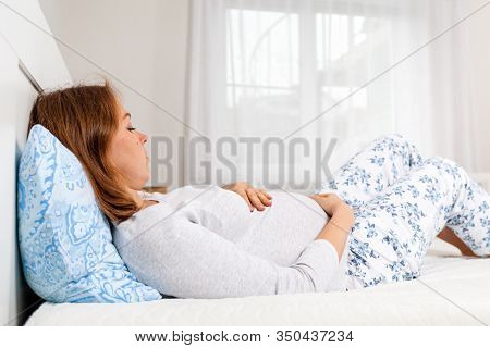 A Tired Pregnant Woman Lies On The Bed And Holds Her Stomach, Worrying About The Upcoming Birth. The