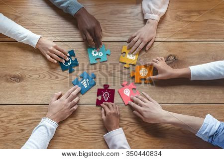 Hands Of International Coworkers Sitting Around Table, Putting Colorful Puzzles Together, Teamwork C