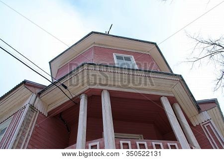 Wooden Two-story House In Dark Pink Color With A Balcony And Columns Against A Blue Cloudy Sky. Bott