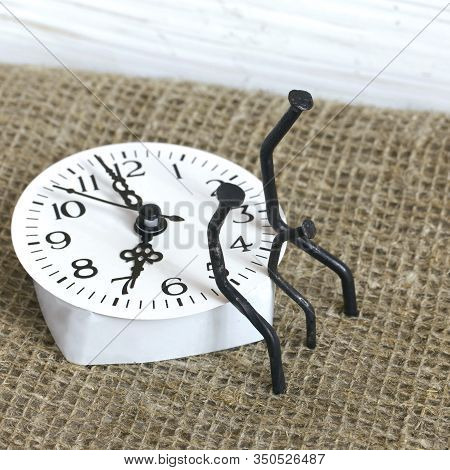 Figurines Of Man Made From Carpentry Nails. They Are Sitting On The Watch Dial, Next To Each Other.