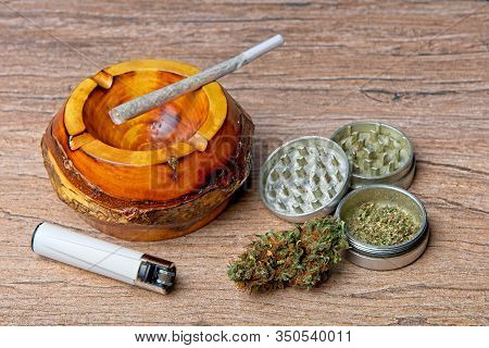 Close Up Of Cannabis - Marijuana Bud And Accessories - Grinder, Wooden Ashtray, Lighter And Rolled J