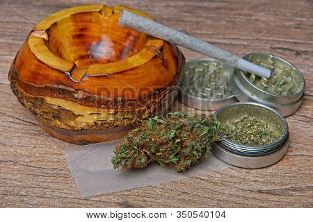 Close Up Of Cannabis - Marijuana Bud And Accessories - Grinder, Wooden Ashtray, Rolling Paper And Ro