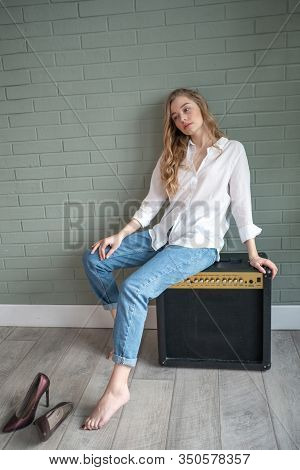 Young Beautiful Woman Sitting On Subwoofer With Bare Feet Next To Green Plant