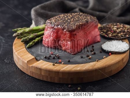 Slice Of Raw Beef Topside Joint With Salt And Pepper On Stone Chopping Board With Fork And Knife, As