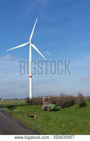 Sint Gillis Waas, Belgium January 16, 2020, Windmill On The Edge Of A Pear Field With A Tractor With
