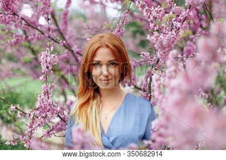 Beautiful Smilling Redhead Woman In Spring Time Blossom Cherrytrees Garden.