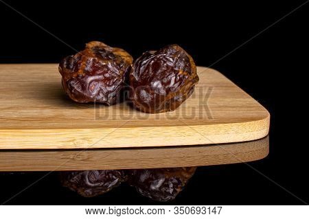 Group Of Two Whole Dry Brown Date Fruit On Bamboo Cutting Board Isolated On Black Glass