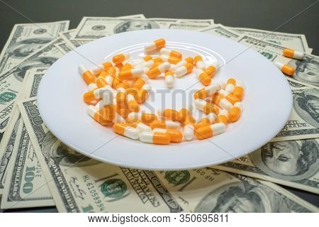 White Plate With Orange-and-white Tablets On The Table With Dollar Bills. Photos Of Falling Tablets 