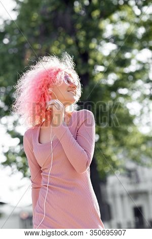 Happy Woman With Curly Pink Hair And Sunglasses Near The Blossoming Spring Tree Listening Music On S