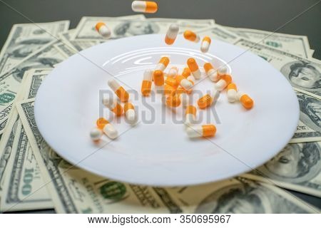 White Plate With Orange-and-white Tablets On The Table With Dollar Bills. Photos Of Falling Tablets 