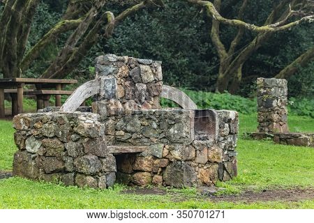 Huge Stone Barbecue For Cooking Meat, Seafood During The Holidays. Benches, A Wooden Table For Food,