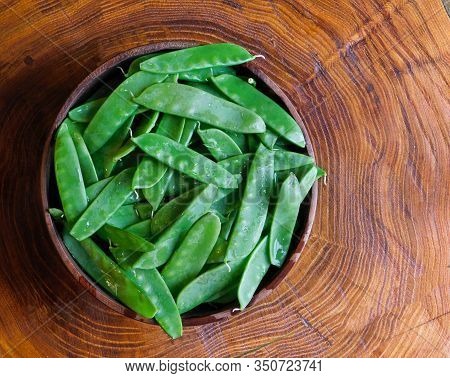 Fresh, Damp Snow Peas In A Wooden Bowl, Sitting On A Tree Trunk Section With Distinct Tree Rings, Na