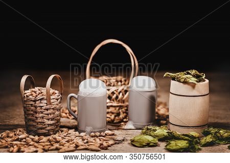 Dried Hop Cones And Malted Barley On Baskets, Beer Mugs, Ingredients For Brewing Beer At Home Or In 