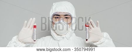 Panoramic Shot Of Asian Epidemiologist In Hazmat Suit And Respirator Mask Showing Test Tubes With Bl