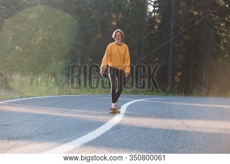 Summer Road Trip. Beautiful Landscape And View Of A Mountain Road. Girl Rides On A Skateboard At The