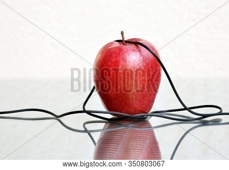 Red Ripe Apple And Thin Electrical Headphones Wire Against A High Key Background With Amazing Reflec