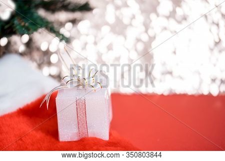 Christmas White Gift Box With A Large Bow Standing On Red Hat Santa Calus Against A Background Bokeh