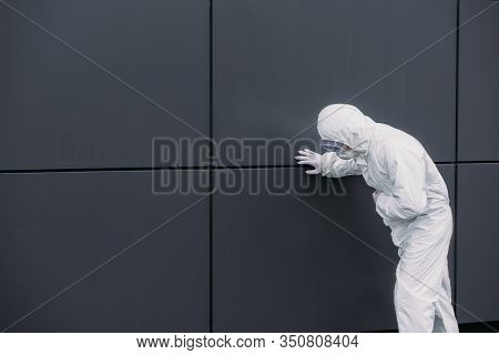 Asian Epidemiologist In Hazmat Suit Leaning On Wall While Suffering From Symptomatic Abdominal Pain