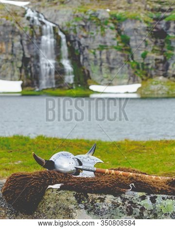 Viking Helmet With Axe On Lake Shore In Norway. Tourism And Traveling Concept