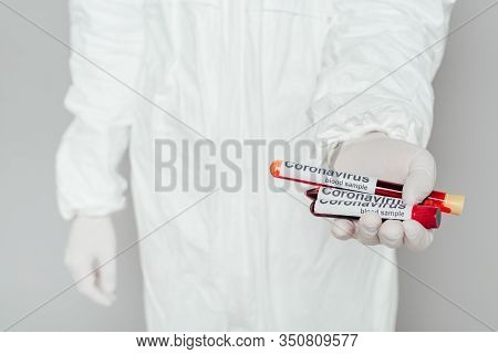 Partial View Of Epidemiologist In Hazmat Suit Showing Test Tubes With Blood Samples On Grey Backgrou