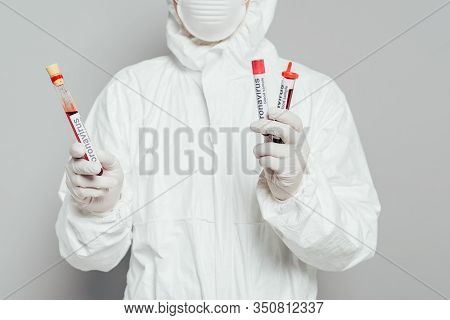 Partial View Of Epidemiologist In Hazmat Suit Holding Test Tubes With Blood Samples On Grey Backgrou