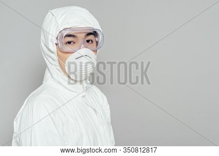 Asian Epidemiologist In Hazmat Suit And Respirator Mask Looking At Camera Isolated On Grey