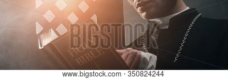 Cropped View Of Catholic Priest Reading Bible In Dark Near Confessional Grille With Rays Of Light, P