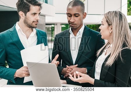 Two Business Colleagues Discussing Reports While Team Leader Making Decision. Man With Papers And Wo