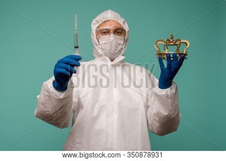 A Male Doctor In Protective Overalls And A Mask Holds An Syringe With A Vaccine And Crown In His Han