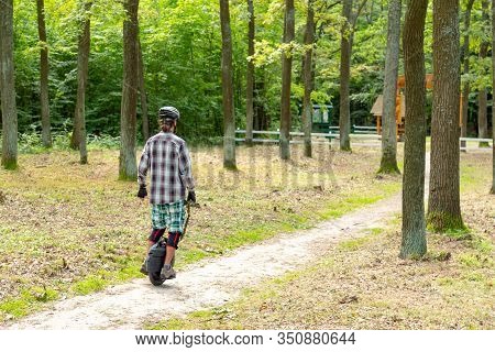 Hipster In Rpotective Wear Riding A Ballance One Wheel Electric Schooter At The Nature Reserve.
