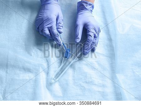 Doctor Holding Anoscope On Light Blue Fabric, Top View. Hemorrhoid Treatment
