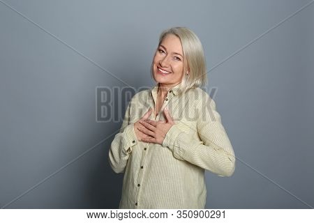 Happy Woman Holding Hands Near Heart On Grey Background