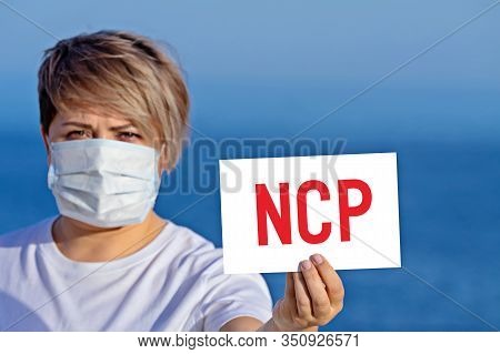 Woman In Surgical Face Mask Holds Blank With Text Ncp That Mean Novel Coronavirus Pneumonia. Concept