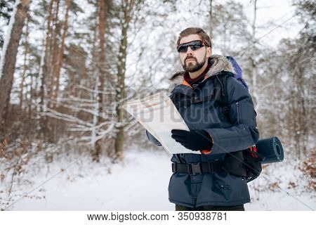 Hiker Checking Map To Orientate In Snow-clad Forest
