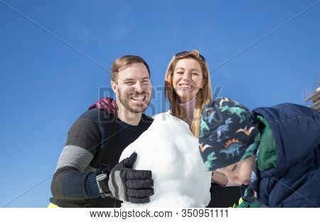 Parents With Child Playing On Snow, Making Snowman. Winter Family Vacation